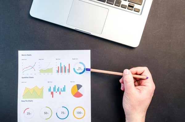 Hand reviewing printed data charts next to a laptop