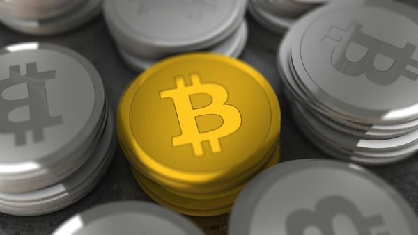 Gold Bitcoin coin standing out among stacked silver coins