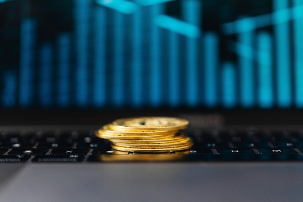 Stacked gold cryptocurrency coins on a laptop keyboard with a bar chart in the background